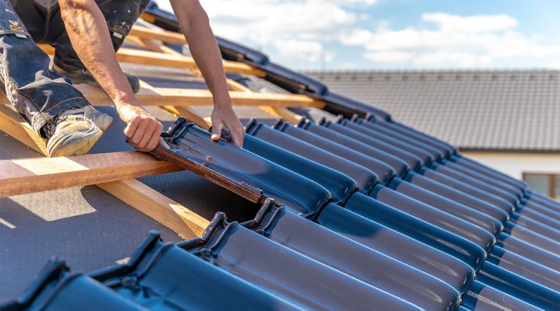 Worker installing glossy clay roofing tiles on a wooden roof structure during a sunny day.