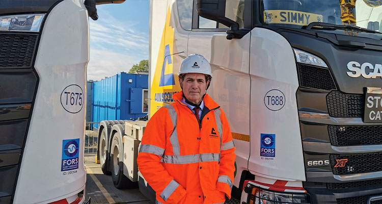 a man in a hard hat and high-visibility jacket standing between two Scania trucks