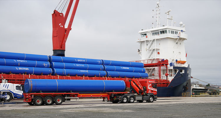 large steel pipes being offloaded at a port from a cargo vessel