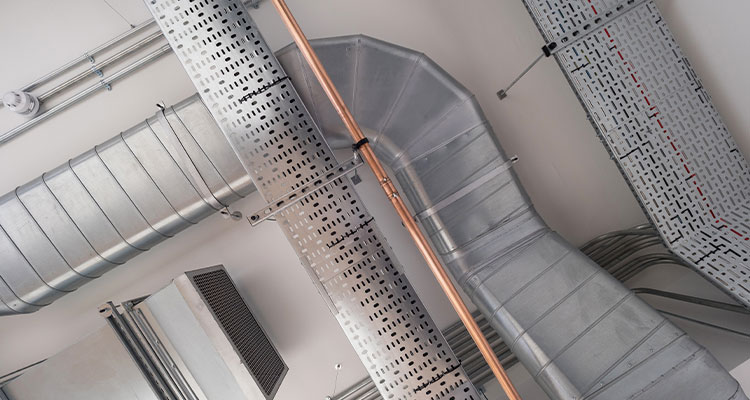 a complex network of mechanical and electrical systems, including various types of ductwork, pipes, and cable trays, installed on a ceiling