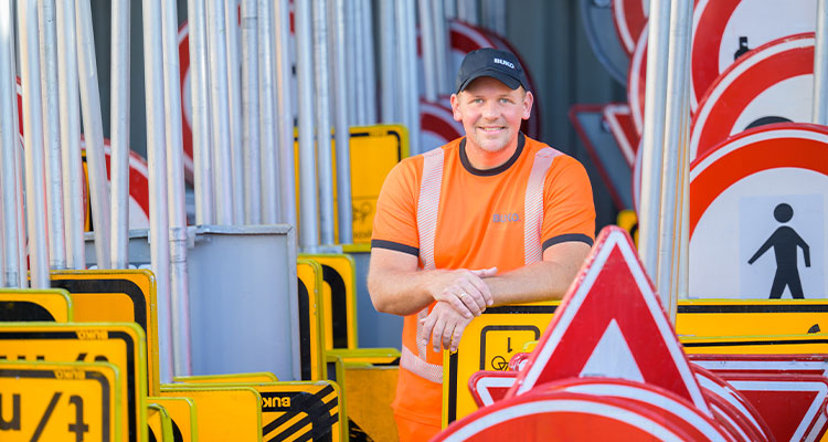 Buko worker in orange High vis standing amongst road safety signs