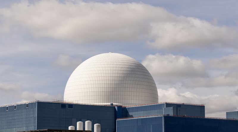 Construction site of a large-scale nuclear reactor in the UK with cranes, steel structures and engineering teams working under cloudy skies