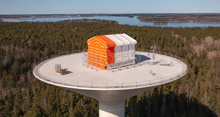 a temporary, house-shaped scaffolding and weather protection structure, installed on top of a water tower